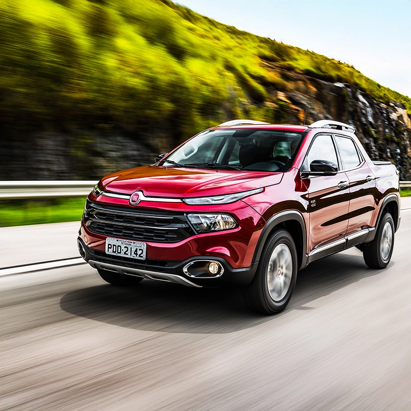 Fiat Toro na cor vermelha transitando em via pavimentada, com vegetação e árvores ao redor. Fiat Toro na cor vermelha transitando em via pavimentada, com vegetação e árvores ao redor.