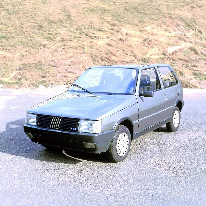 Fiat Uno prata fotografado de frente em ambiente externo, com destaque para o design marcante da primeira geração. Fiat Uno prata fotografado de frente em ambiente externo, com destaque para o design marcante da primeira geração.